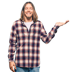 Wall Mural - Handsome caucasian man with long hair wearing hipster shirt smiling cheerful presenting and pointing with palm of hand looking at the camera.