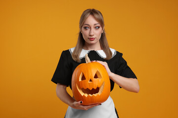 Canvas Print - Woman in scary maid costume with carved pumpkin on orange background. Halloween celebration