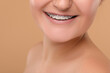 Happy woman with dental braces on brown background, closeup