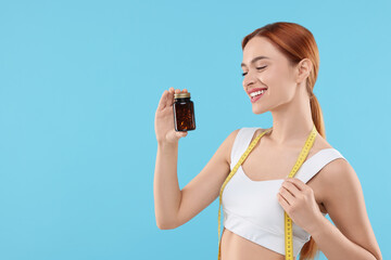 Poster - Happy young woman with bottle of pills and measuring tape on light blue background, space for text. Weight loss