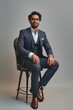 Happy successful rich young indian business man ceo leader, wealthy arab professional manager, confident male businessman executive wearing suit sitting on chair isolated on beige, Generative AI