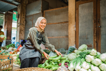 Wall Mural - asian hijab vegetable seller looking at camera while arranging greengroceries at her stall