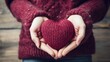 Close-up of a woman in a warm sweater holding a knitted burgundy heart in her hands. Valentine's Day greeting card. A symbol of love.
