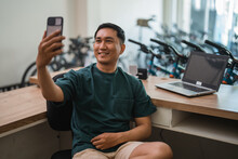 young man taking a selfie with his cell phone while working at his desk