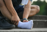 Fototapeta  - Sportsman touching his sore ankle, injured while training running workout in public park