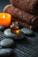 Poster - A bottle of oil sits on top of rocks next to a candle. This versatile image can be used to depict relaxation, aromatherapy, or a peaceful atmosphere