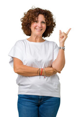 Wall Mural - Beautiful middle ager senior woman wearing white t-shirt over isolated background with a big smile on face, pointing with hand and finger to the side looking at the camera.