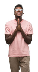 Canvas Print - Young african american man wearing pink t-shirt praying with hands together asking for forgiveness smiling confident.