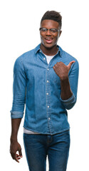 Canvas Print - Young african american man over isolated background smiling with happy face looking and pointing to the side with thumb up.