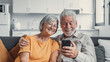 © Daniel - Happy mature family, wife and husband using phone together at home, smiling middle aged man and woman sitting on couch, using mobile device apps, watching video in social network, surfing internet.