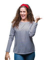 Poster - Beautiful brunette curly hair young girl wearing stripes sweater over isolated background smiling with happy face looking and pointing to the side with thumb up.