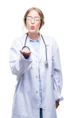 Canvas Print - Beautiful young blonde doctor woman wearing medical uniform over isolated background looking at the camera blowing a kiss with hand on air being lovely and sexy. Love expression.