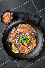 Wall Mural - Fresh Salmon carpaccio with onion and arugula on a plate. Black background. Top view