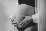 Fototapeta  - Closeup belly of a woman. Pregnancy motherhood procreation concept. Pregnant female waiting for newborn baby. Young girl touching and holding belly, caring about health indoors. Black and white photo