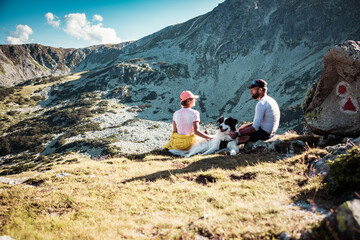 Poster - couple with dog sitting on rocks admiring mountain landscape slow travel