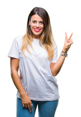 Wall Mural - Young beautiful woman casual white t-shirt over isolated background smiling with happy face winking at the camera doing victory sign. Number two.