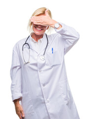 Poster - Middle age blonde doctor woman over isolated background smiling and laughing with hand on face covering eyes for surprise. Blind concept.