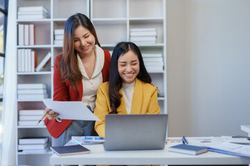 Wall Mural - Two happy asian businesswoman talking and using a laptop computer in a meeting.