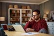 © Jelena - A busy young adult male freelancer resting his head on his hand while working on a project on a laptop.