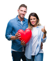 Wall Mural - Young couple in love holding red heart over isolated background happy with big smile doing ok sign, thumb up with fingers, excellent sign