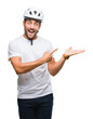 Young handsome man wearing cyclist safety helmet over isolated background amazed and smiling to the camera while presenting with hand and pointing with finger.