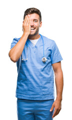 Wall Mural - Young handsome doctor surgeon man over isolated background covering one eye with hand with confident smile on face and surprise emotion.