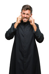 Canvas Print - Young catholic christian priest man over isolated background covering ears with fingers with annoyed expression for the noise of loud music. Deaf concept.