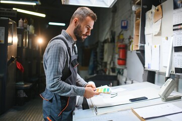 Wall Mural - Print house worker controlling printing process quality and checking colors with magnifying glass