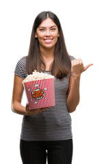 Poster - Young beautiful hispanic eating popcorn pointing and showing with thumb up to the side with happy face smiling