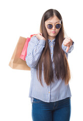 Sticker - Young Chinese woman over isolated background holding shopping bags on sales with angry face, negative sign showing dislike with thumbs down, rejection concept