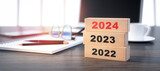 Fototapeta Dmuchawce - 3D render of a stacked wooden blocks with year number 2022 2023 2024 on a office workplace background - 3D illustration