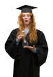 © Krakenimages.com - Young redhead student woman wearing graduated uniform holding hourglass scared in shock with a surprise face, afraid and excited with fear expression