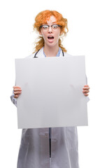 Canvas Print - Young redhead doctor woman holding banner scared in shock with a surprise face, afraid and excited with fear expression