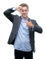 Wall Mural - Young handsome blond business man smiling making frame with hands and fingers with happy face. Creativity and photography concept.