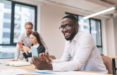 Sticker - Cheerful black man using smartphone in office