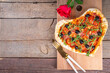 Valentines day heart shaped pizza, love and dating concept with mozzarella. tomatoes, pepperoni and arugula on vintage wooden table background top view copy space