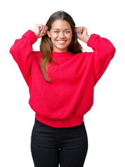 Sticker - Young beautiful brunette woman wearing red winter sweater over isolated background Smiling pulling ears with fingers, funny gesture. Audition problem