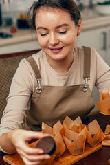 Wall Mural - A young woman packs cupcakes in a craft box. the concept of food delivery. A birthday package. small business. The bakery chef bakes pastries and cakes in the kitchen