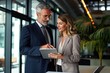 © Lumina Frame - Two busy older professional corporate business executives man and woman wearing suits holding tablet technology device having discussion working on digital project plan standing in office,GenerativeAI