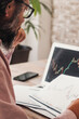© simona - Worried and thoughtful man study stock exchange crypto charts on paper and computer display. Concept of economy and money investment on forex exchange. Making or losing money with online business