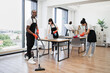 © sofiko14 - Team of multicultural cleaners wipes tables and gadgets, shelves, washes windows in spacious, bright, modern office. Side view of African American man using vacuum cleaner to clean floor from dirt.