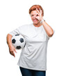 Atrractive senior caucasian redhead woman holding soccer ball over isolated background with happy face smiling doing ok sign with hand on eye looking through fingers
