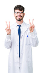 Wall Mural - Young professional scientist man wearing white coat over isolated background smiling looking to the camera showing fingers doing victory sign. Number two.