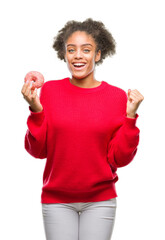 Canvas Print - Young afro american woman eating donut over isolated background screaming proud and celebrating victory and success very excited, cheering emotion