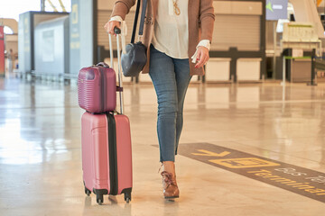  detail of a woman's legs walking with suitcases of luggage through the airport terminal. unrecognizable woman in casual clothes