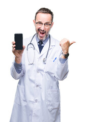 Canvas Print - Middle age senior hoary doctor man showing smartphone screen over isolated background pointing and showing with thumb up to the side with happy face smiling