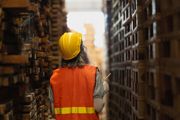 woman worker carpenter wearing safety uniform and hard hat working and checking the quality of wooden products at workshop manufacturing. man and woman workers wood in dark warehouse industry.