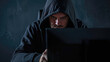 Hacker in a dark hoody sitting in front of a computer. Cybersecurity concept. Dark background