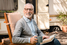 Closeup Photo Of Old Senior Elderly Grandfather Man Adventurer Explorer Relaxing In A Chair Reading Book While Traveling Caravanning In Motor Home Camper Van Trailer