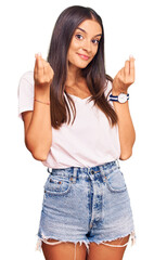 Wall Mural - Young hispanic woman wearing casual white tshirt doing money gesture with hands, asking for salary payment, millionaire business
